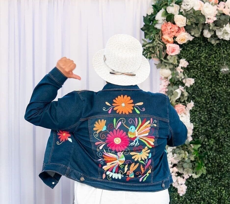 Photo of a woman wearing an embroidered jean jacket, as seen from behind.