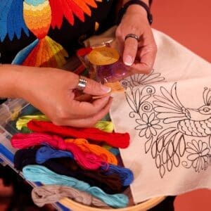 Photo of a woman working on an embroidery project. The outline of the project looks like a bird.