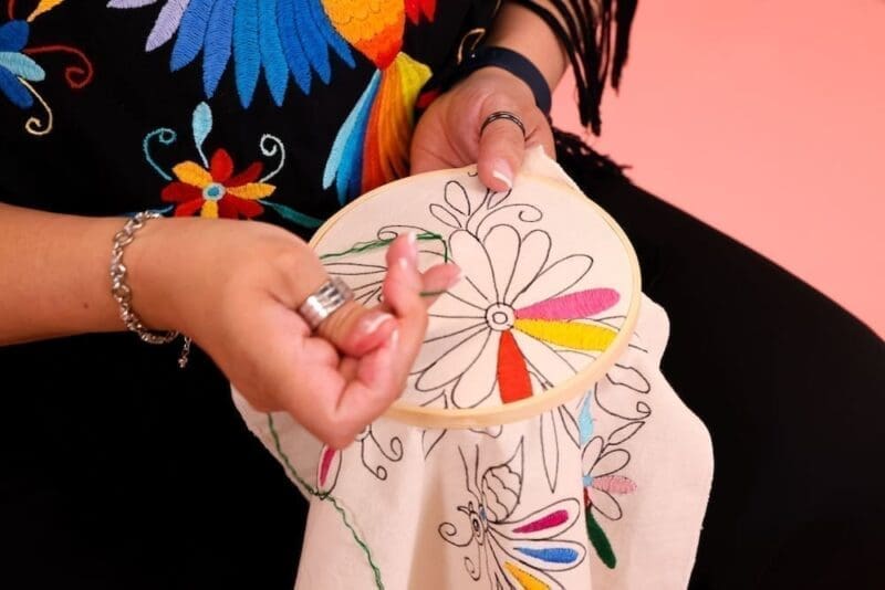 Photo of a woman working on an embroidery project. The outline of the project looks like a flower.