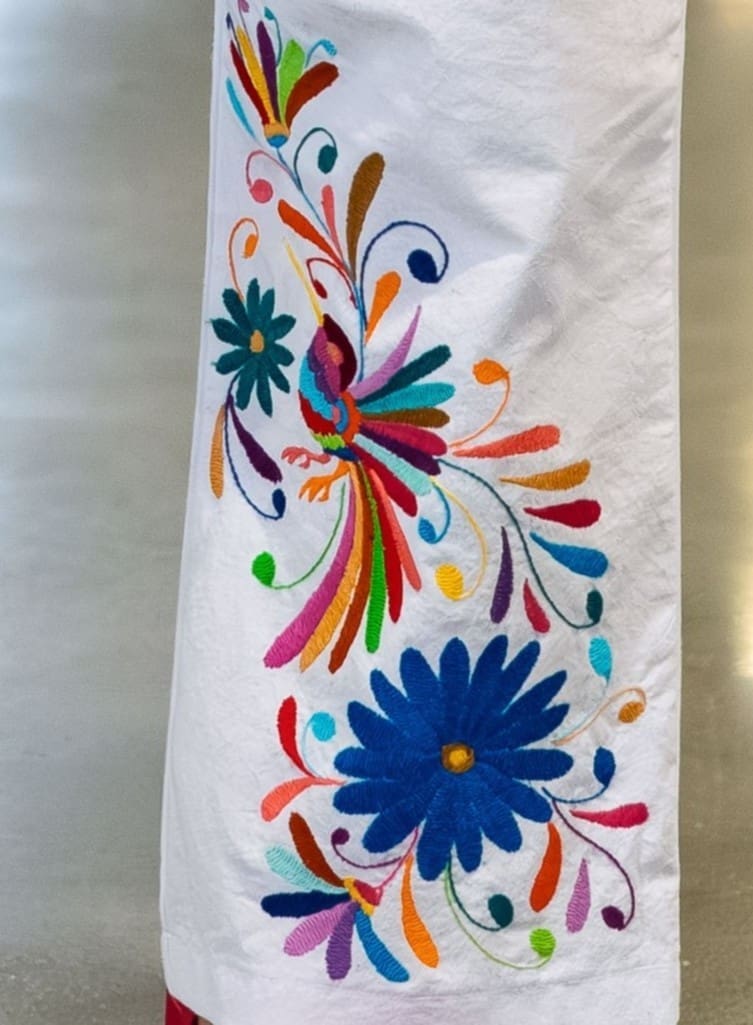 Close-up of multicolor hand-embroidered Otomi bird and large cobalt blue daisy flower with botanical scrolls on white cotton pants fabric
