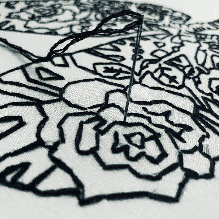 Close up of hand embroidery with a needle and black thread stitching a rose on white fabric in Bentonville, Arkansas. Acercamiento de bordado a mano con aguja e hilo negro delineando una rosa sobre tela blanca en Bentonville, Arkansas.